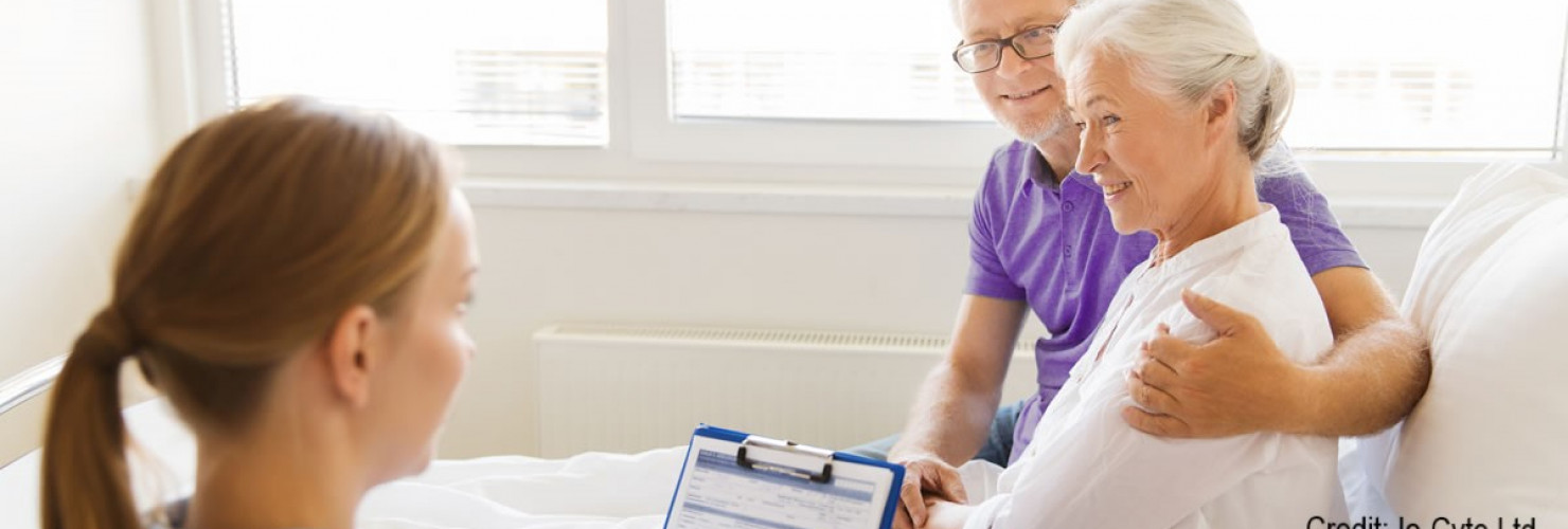 Image of woman on hospital bed being supported by her husband whilst talking to a medical professional