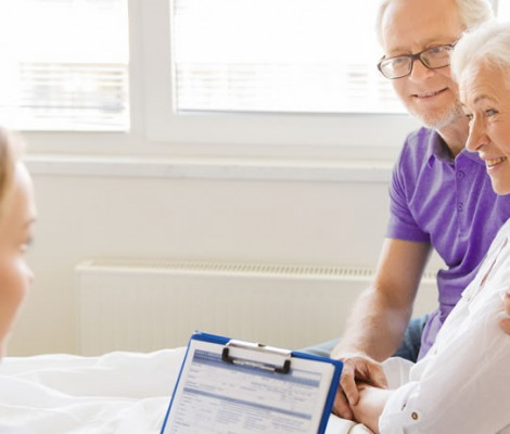 Image of woman on hospital bed being supported by her husband whilst talking to a medical professional